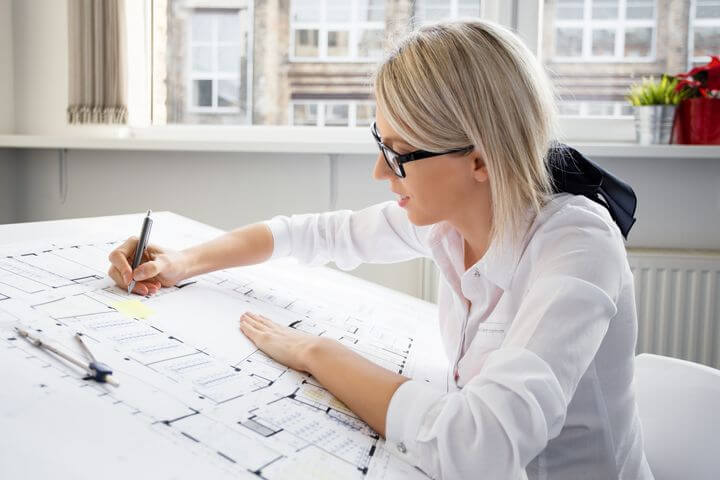 Frau mit Brille zeichnet etwas in einen Plan ein