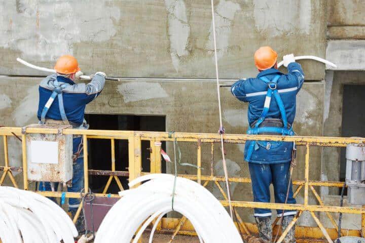 zwei Bauarbeiter mit Helmen arbeiten an einer Wand