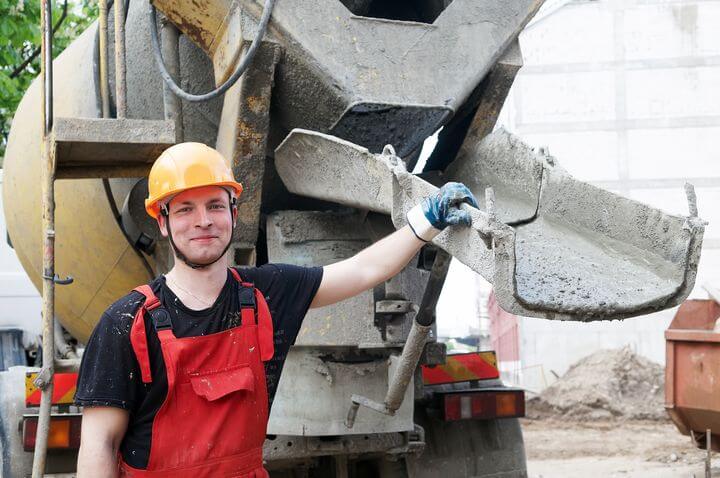 junger Bauarbeiter der sich am Betonmischer anlehnt