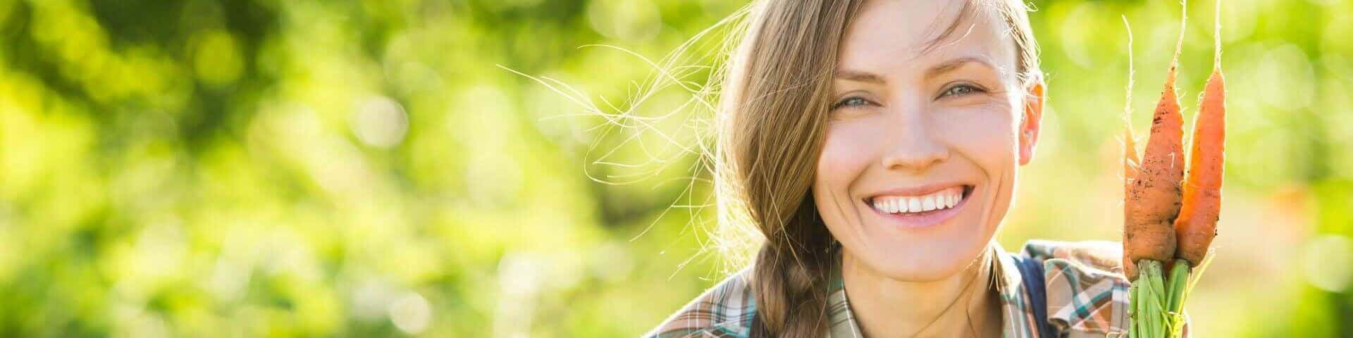 junge Frau lacht mit einer Blume in der Hand in die Kamera