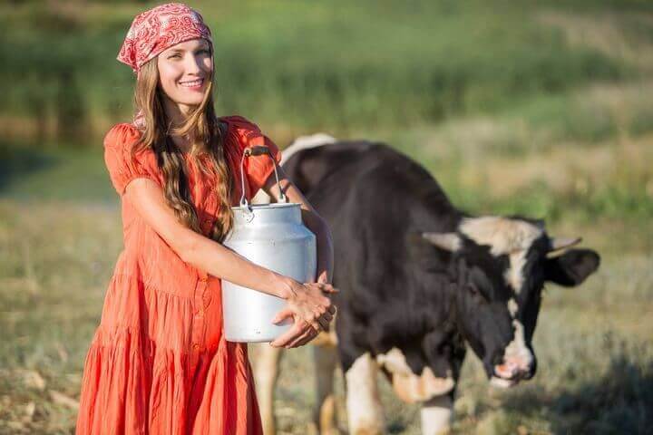 Baeuerin posiert mit einem Milcheimer vor der Kuh