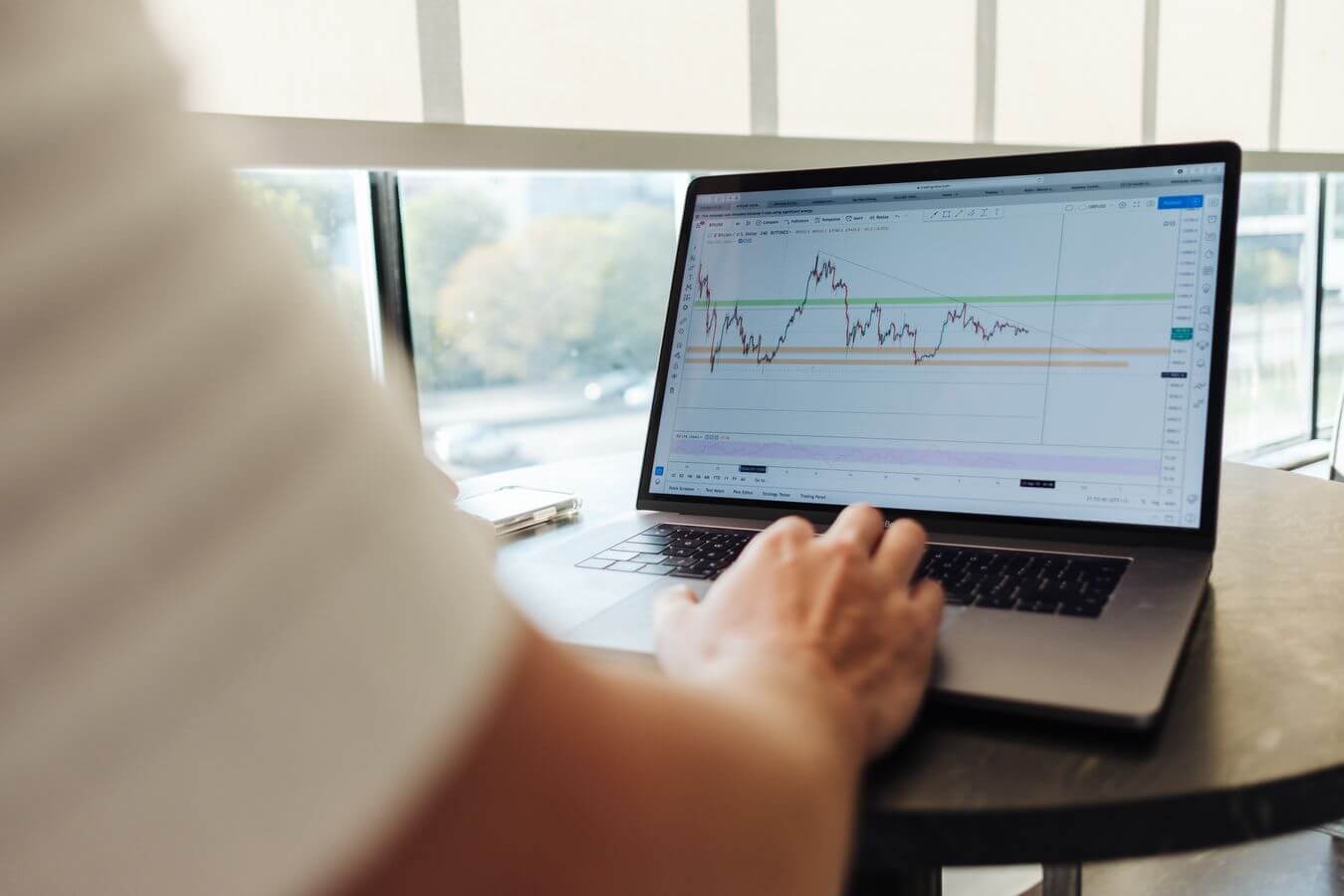 Lehrlingsportal.at Person analysiert in einem sonnendurchfluteten Raum Finanzdiagramme auf einem Laptop.