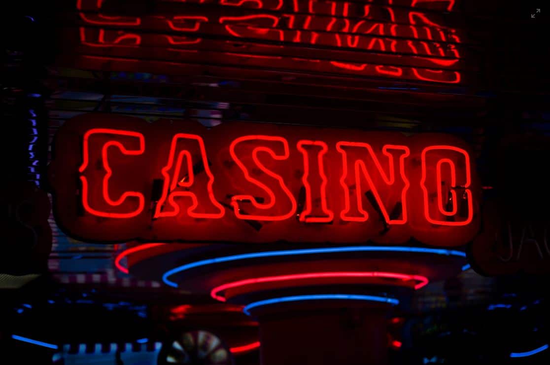 Lehrlingsportal.at Rotes Neonschild mit dem Wort „CASINO“ in einer dunklen Umgebung mit blauen und rosa Lichtakzenten.