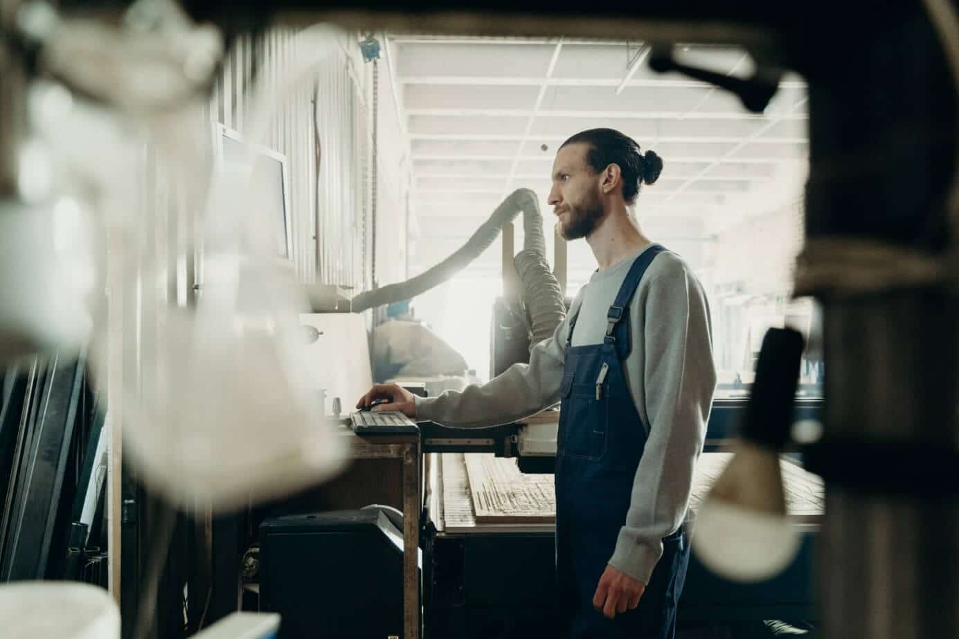 Lehrlingsportal.at Ein Mann im Overall bedient Maschinen in einer Werkstatt. Im Hintergrund sind verschiedene Industriewerkzeuge und -geräte zu sehen.