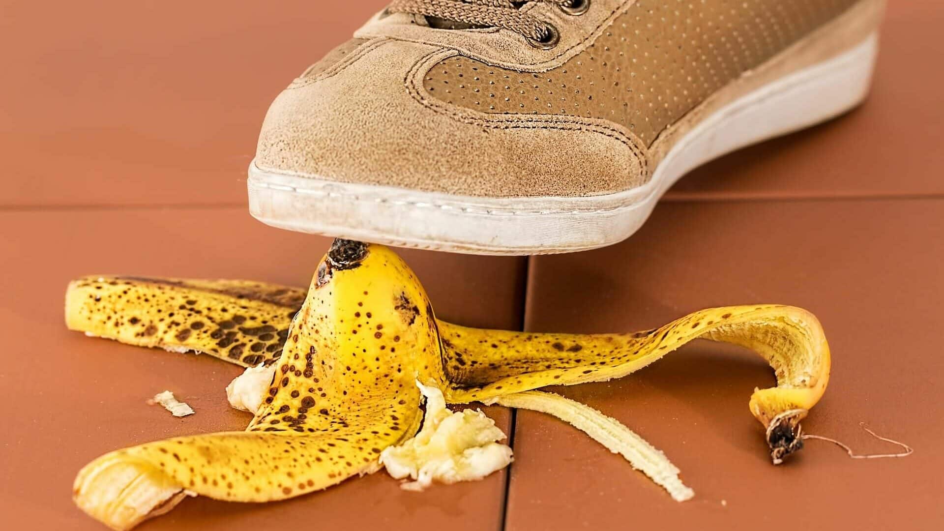 Lehrlingsportal.at Ein Turnschuh, der im Begriff ist, auf eine Bananenschale auf einem gefliesten Boden zu treten.