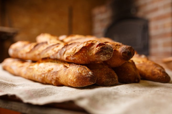 Lehrlingsportal.at Ein Stapel frisch gebackener Baguettes auf einer tuchbedeckten Fläche in rustikalem Ambiente.