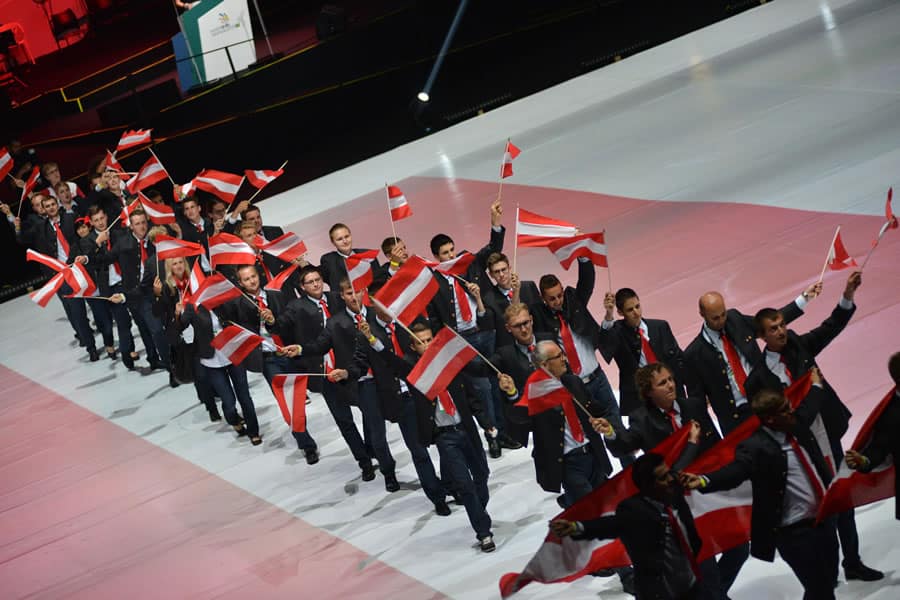 Lehrlingsportal.at Eine Gruppe von Menschen in Abendgarderobe marschiert in einer großen Indoor-Arena und schwenkt rot-weiße Fahnen.