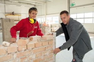 Ausbildner zeigt Lehrling wie man Ziegelwand abmisst