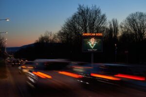 Leuchtreklame auf befahrener Straße Abends