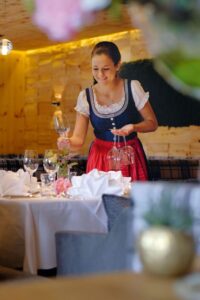 Kellnerin in Dirndl deckt den Tisch mit Weingläsern