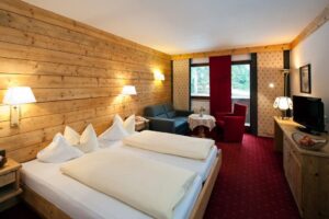 Hotelzimmer mit Doppelbett, TV und gemütlicher Sitzecke mit Holzwand