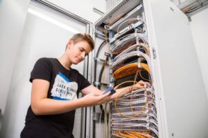 Lehrling mit dunklem T-Shirt prüft Netzwerkkabel