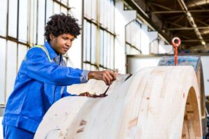 Lehrling in blauer Arbeitskleidung streicht Holzelement