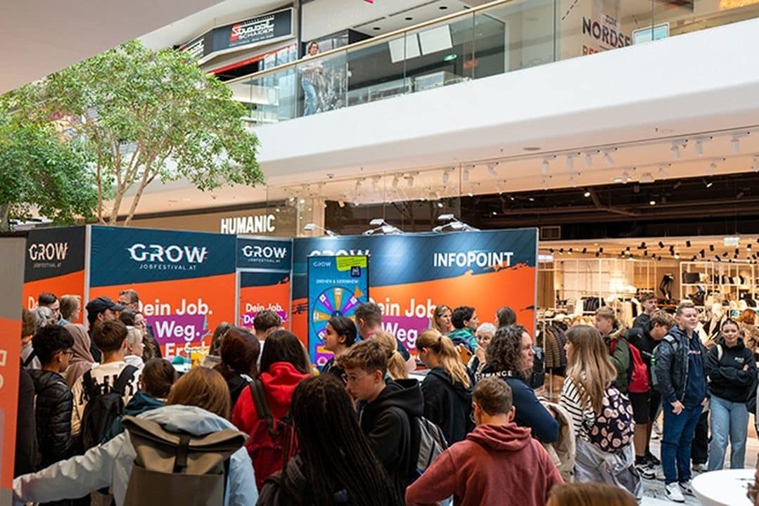 Lehrlingsportal.at Ein gut besuchtes Jobfestival in einem Einkaufszentrum, bei dem sich die Leute unter hellem Licht um Informationsstände versammeln.